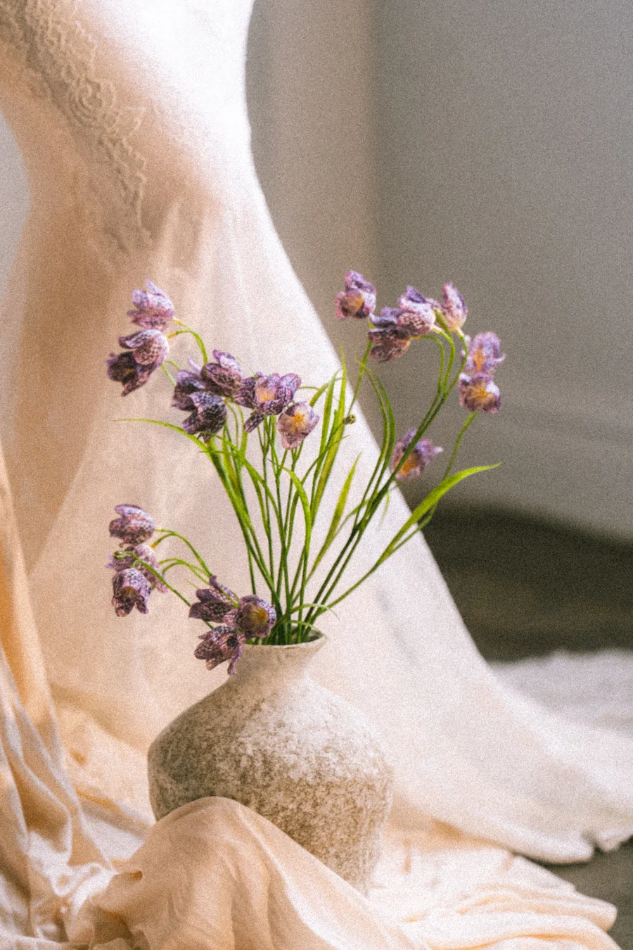 Flowing purple artificial flowers in a rounded ceramic vessel with draped fabric, PO006
